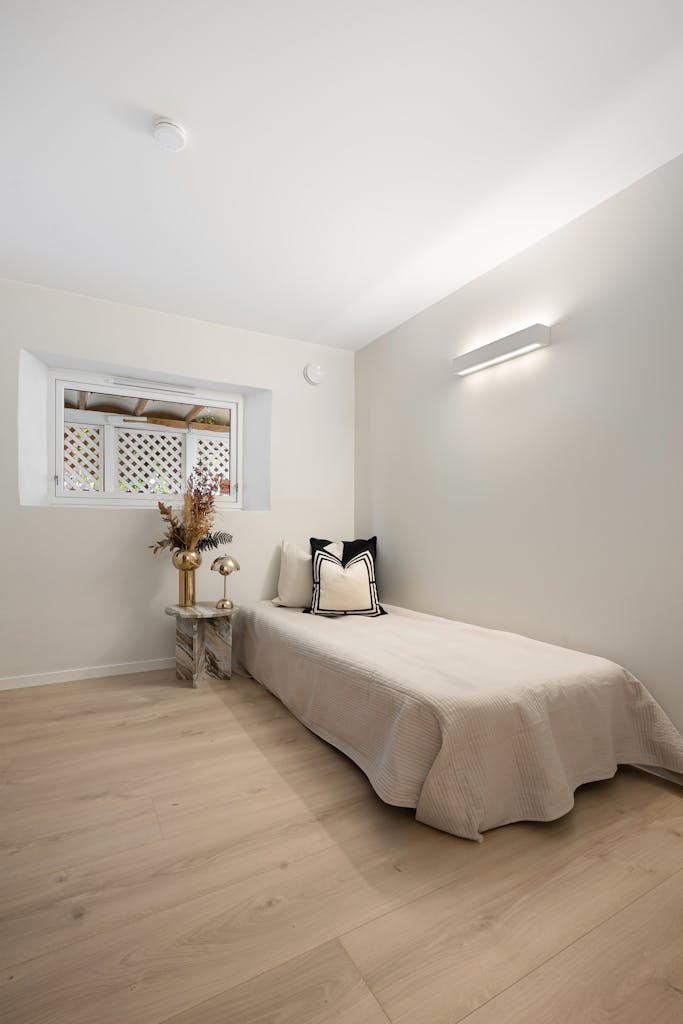 Bright minimalist bedroom featuring a single bed, neutral tones, and wooden flooring.